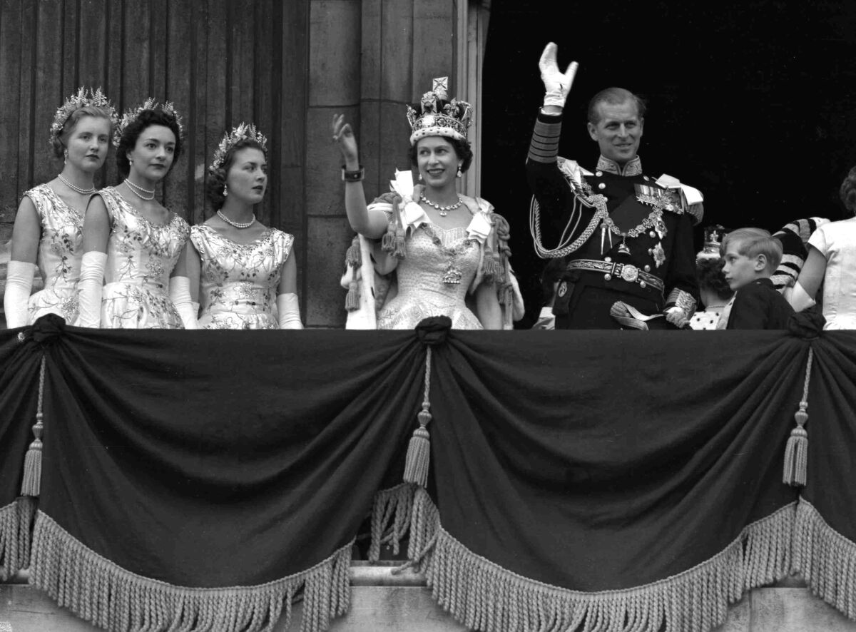 英国女王伊丽莎白二世和菲利普亲王在阳台上挥手致意，三名女士在旁边观看。