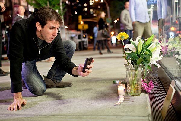 Aaron Katersky takes a picture of candles and flowers that have been placed in remembrance of Steve Jobs outside an Apple Store in New York.