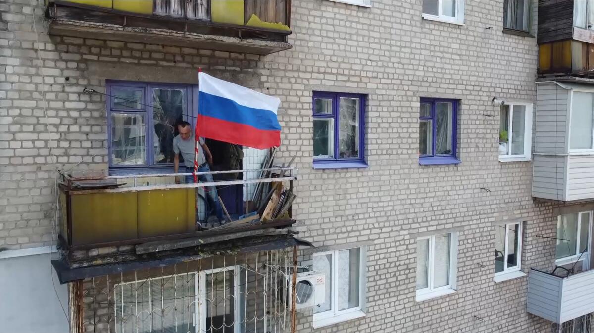 A man sets a Russian national flag on a balcony of a residential building in Lysychansk.