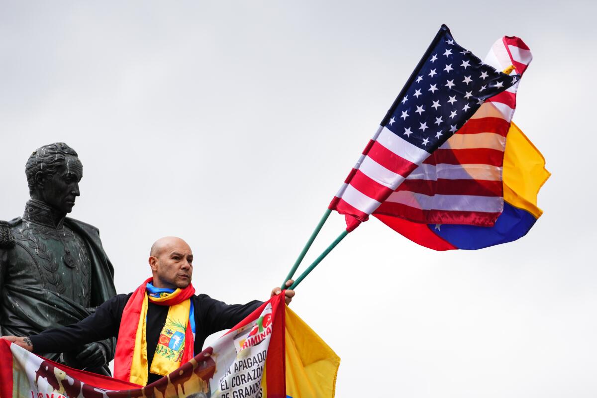 A man holds the flags of Venezuela and the United States next to the statue of Simon Bolivar