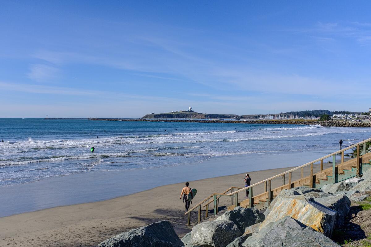 A man with a surfboard walks along a beach.