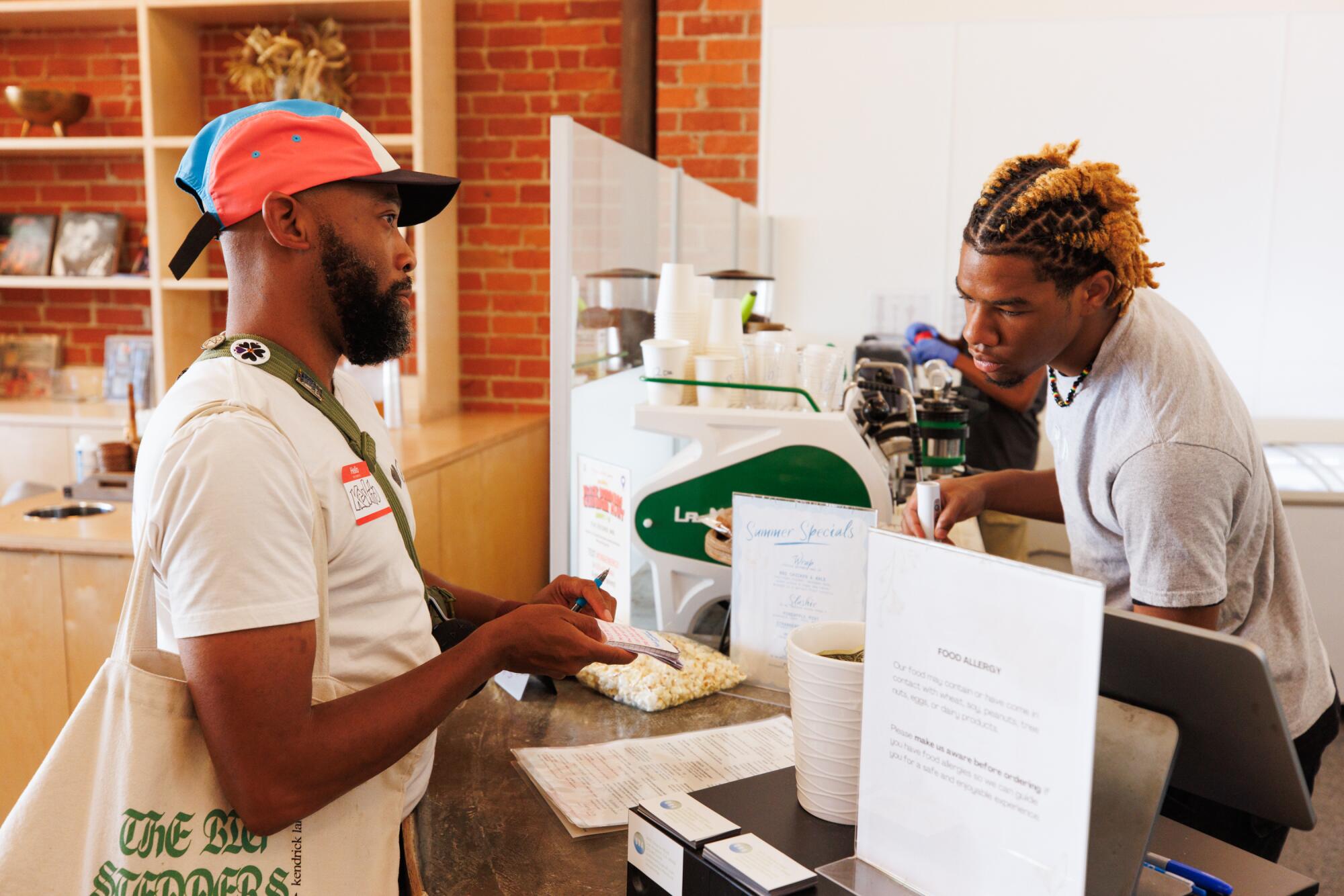 Kevito Clark uses a notepad to communicate with Kimoni Oliver, a barista at ORA.