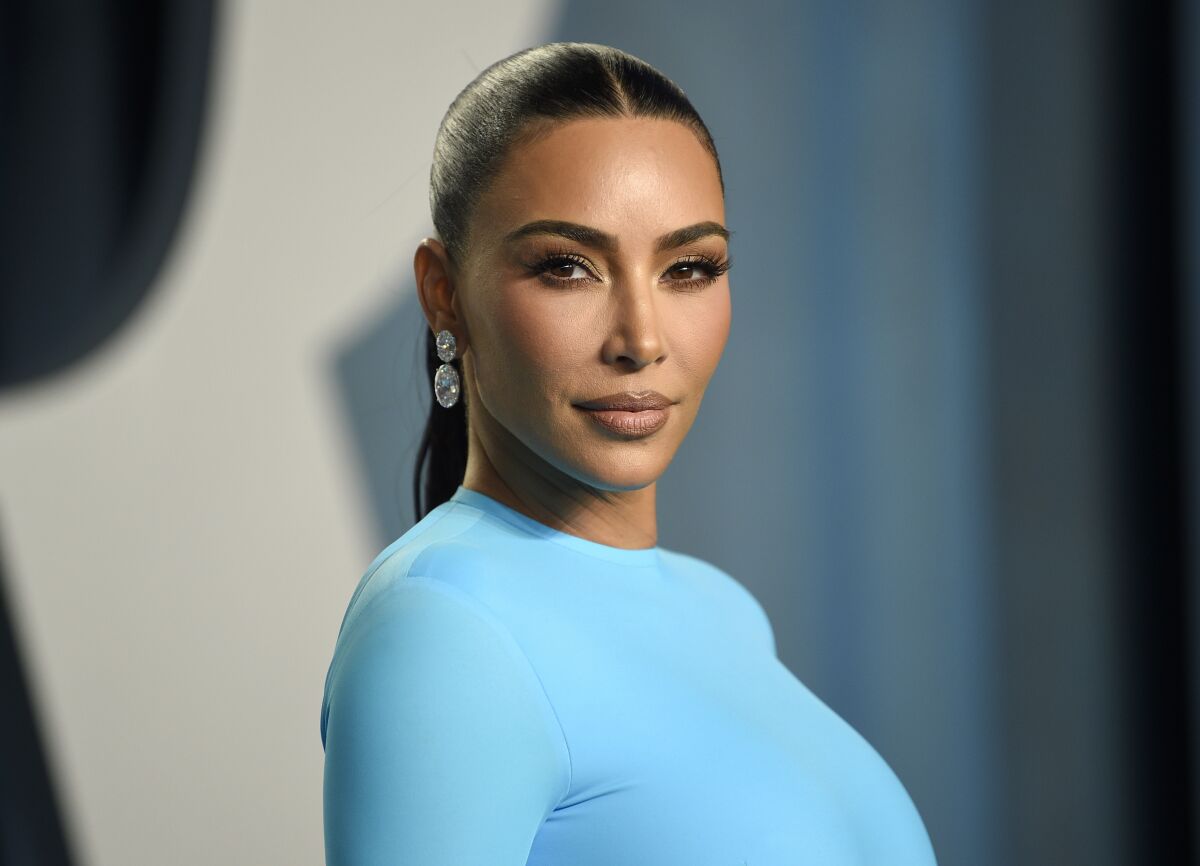 A woman with slicked back hair poses for the camera in a light blue dress