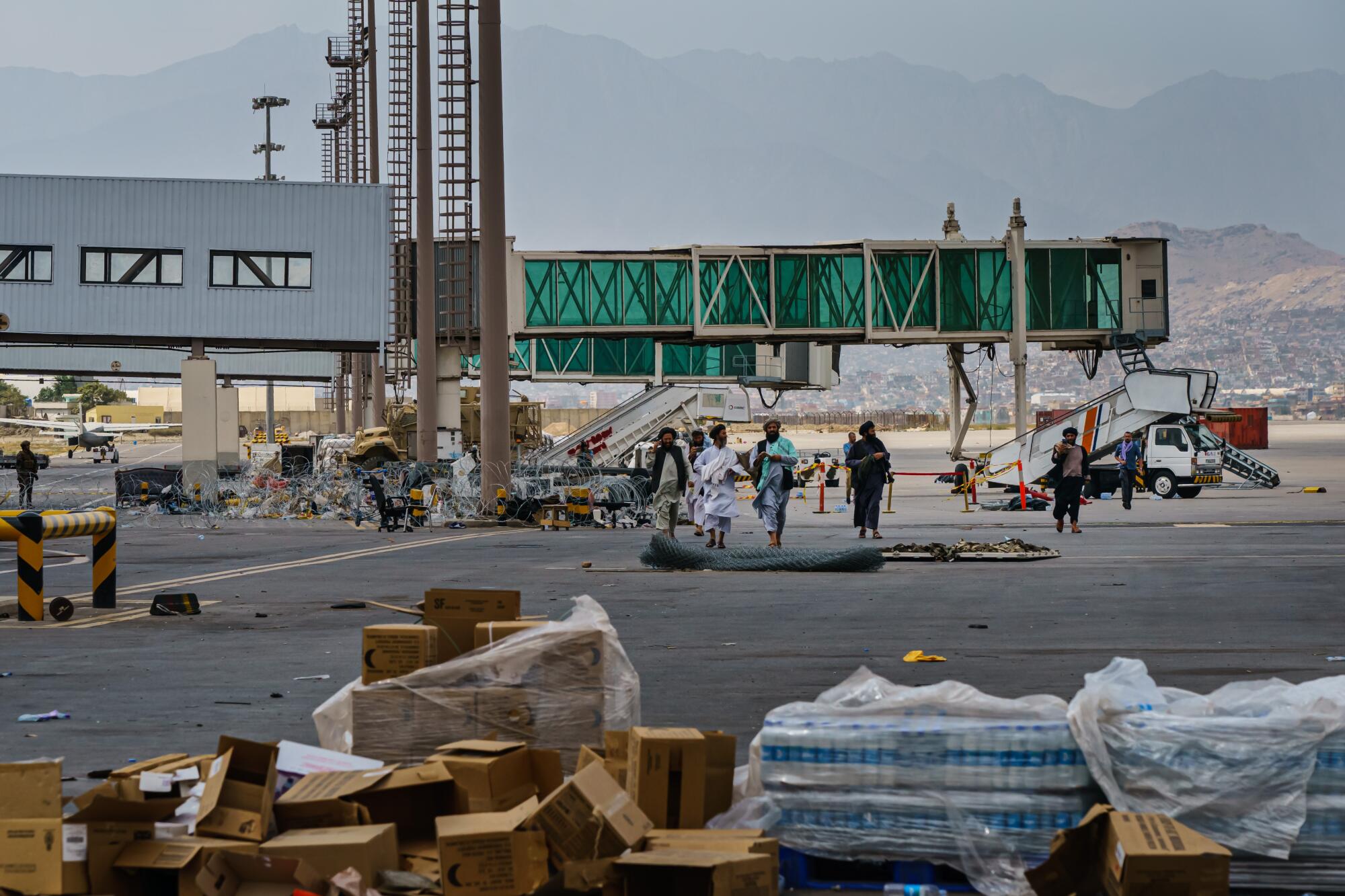 Taliban fighters walk toward stacks of bottled water and other supplies left on the tarmac at the Kabul airport