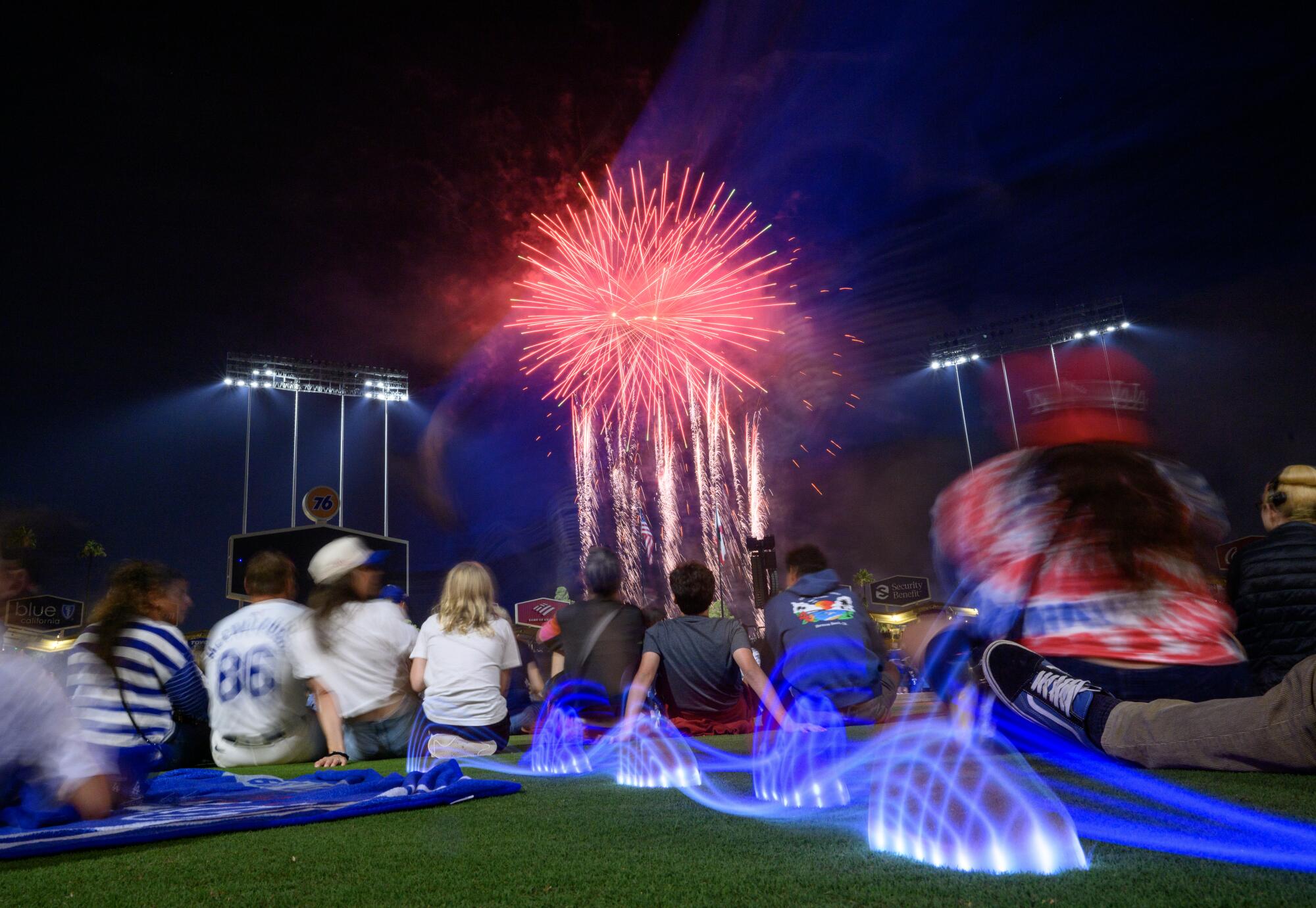 Un joven con luces azules en sus zapatillas corre por el campo mientras se muestran fuegos artificiales sobre el Dodger Stadium.