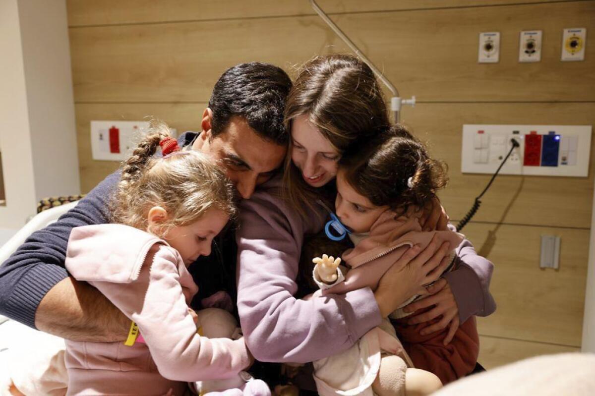 A couple and their daughters embrace in a hospital room 