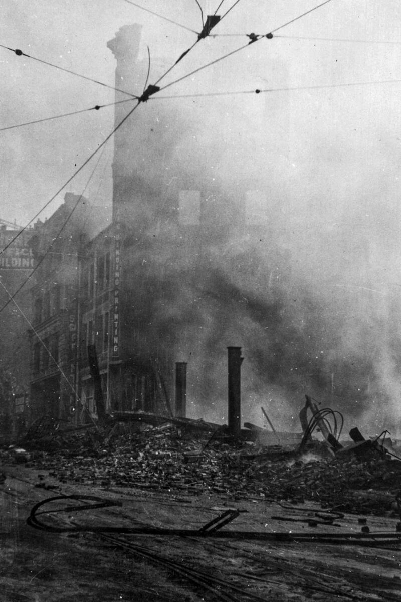A black-and-white photo shows smoke rising from the charred remains of a building 