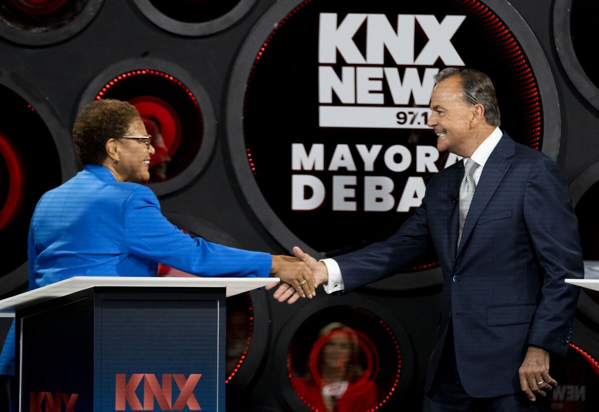 A woman in a bright blue jacket and a man in a dark suit reach out on a stage with a podium.