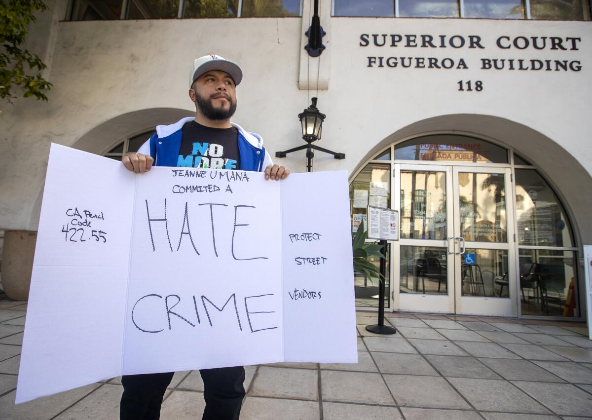 A man stands outside a building holding a sign that reads in part, "Hate Crime"