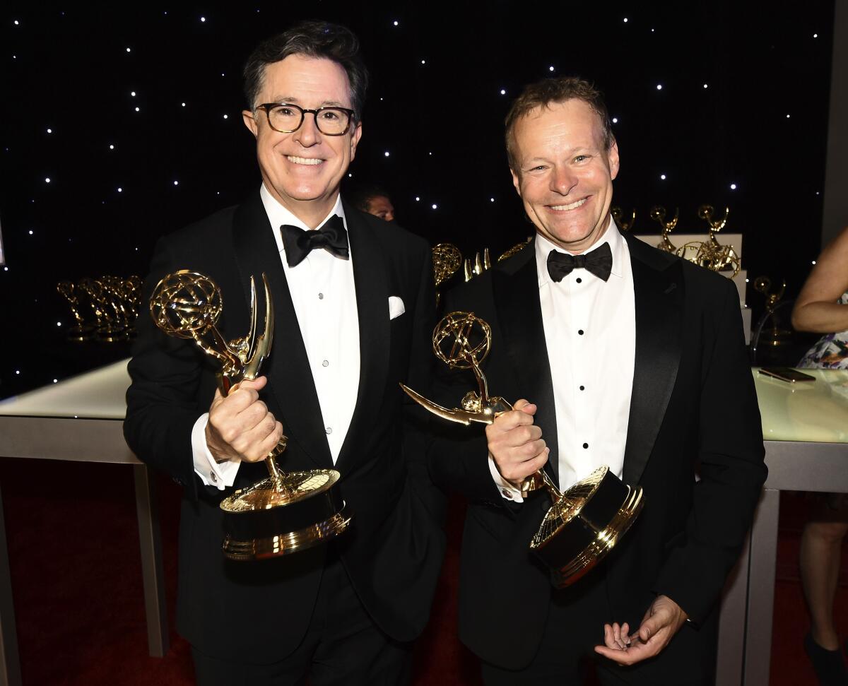 Two men men in tuxes smile holding emmys 