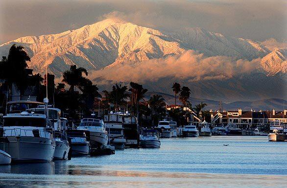 The setting sun and clearing clouds reveal the snow-capped San Gabriel Mountains as viewed from a boat in Huntingon Harbour on Monday.