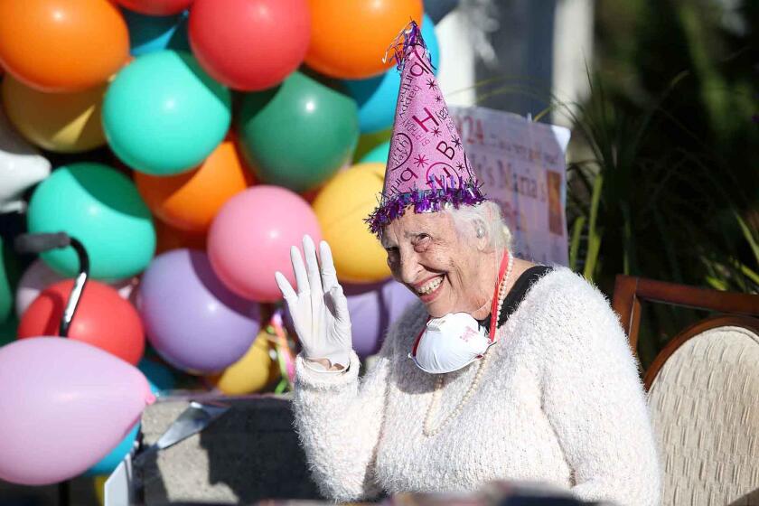 Maria Siani waives to friends and family as she is greeted with drive-by surprise 96th birthday party on the street in front of her home in Laguna Beach.