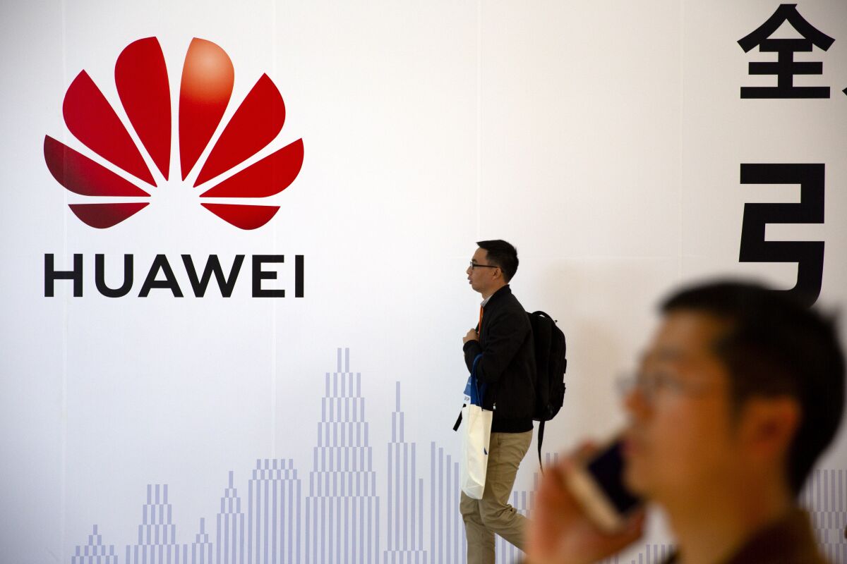 In this Oct. 31, 2019 photo, man uses his smartphone as he stands near a billboard for Chinese technology firm Huawei at the PT Expo in Beijing. Chinese tech giant Huawei kept its global business growing for almost a decade while Washington piled sanctions on the company and lobbied its allies to keep the company out of telecom networks. Now, Huawei is starting to suffer in earnest as the Trump administration steps up efforts to slam the door on access to Western components and markets in a widening feud with Beijing over technology and security. (AP Photo/Mark Schiefelbein)