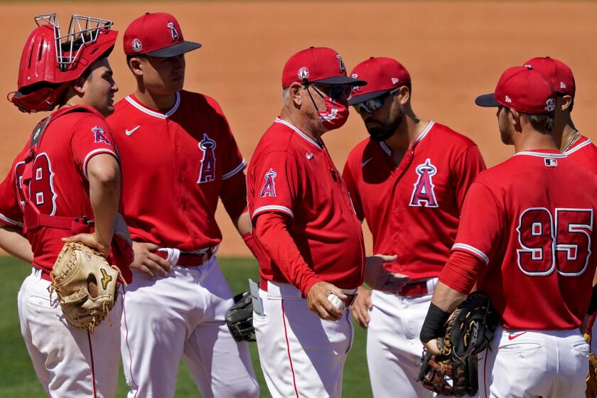 Los Angeles Angels manager Joe Maddon, center, speaks with his players during a pitching change during the fourth inning of a spring training baseball game against the San Diego Padres, Saturday, March 27, 2021, in Tempe, Ariz. (AP Photo/Matt York)