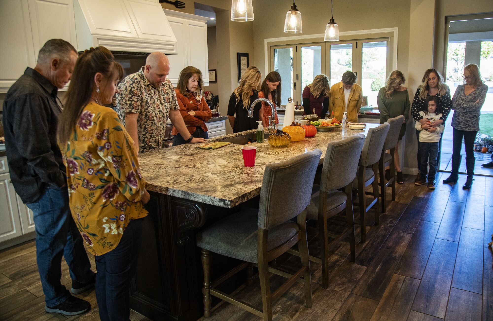 A dozen Barnard family members stand around a marble-topped kitchen island with their heads bowed.