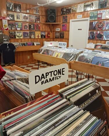 Wooden shelves and trays full of vinyl records in a shop, one area labeled Daptone Family.
