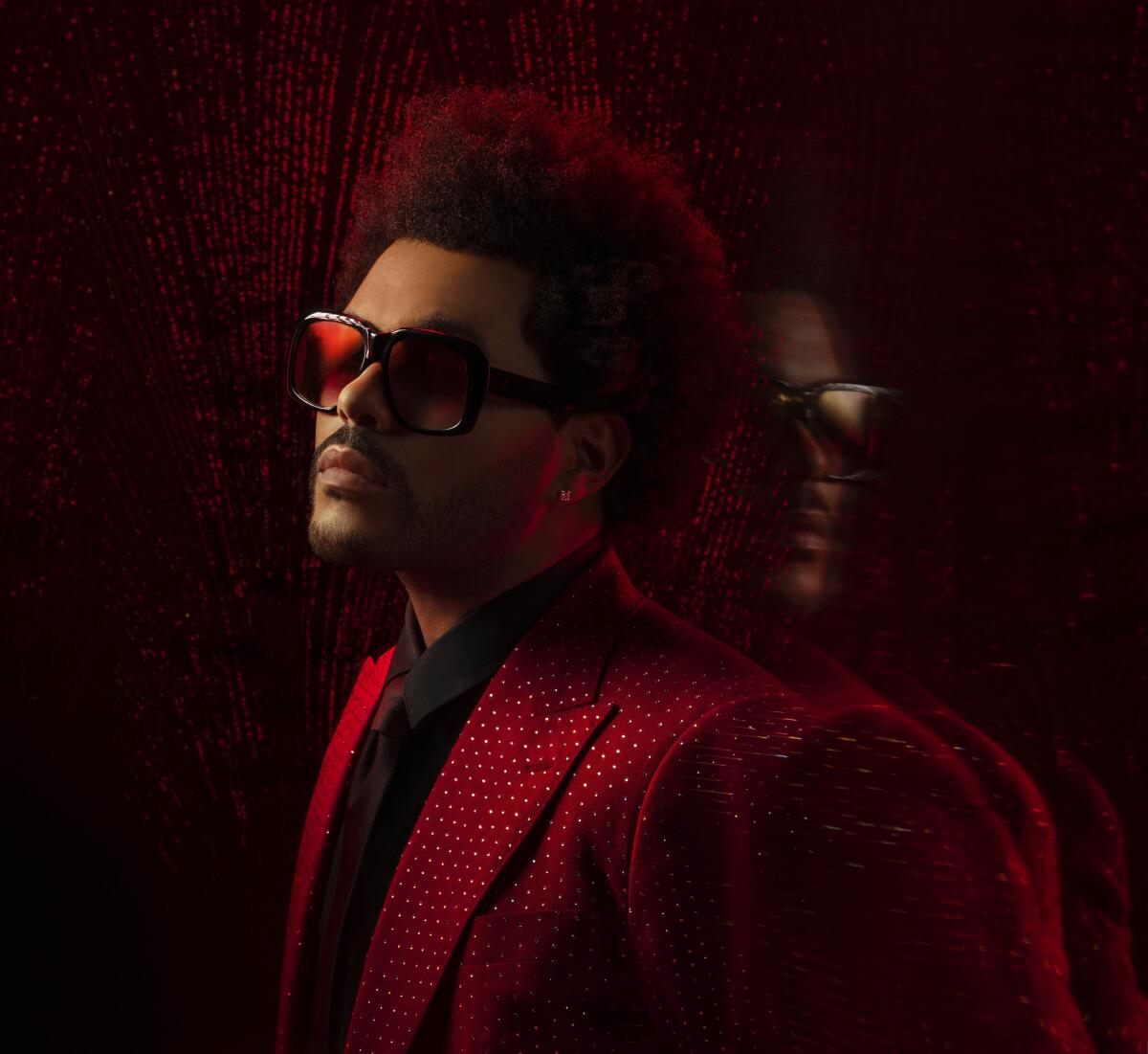 The Weeknd in a red sparkly suit leaning on a mirrored wall