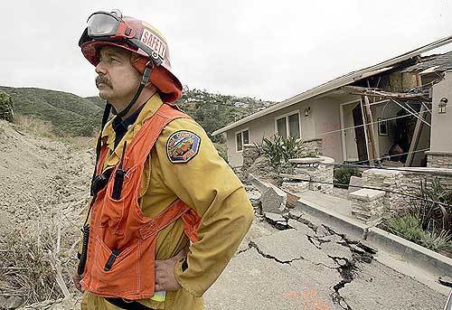 Orange County Fire Authority Captain Bret J. Russell stands watch over the red zone in Bluebird Canyon. The home behind Russell on Flamingo Road was torn in two by the slide.