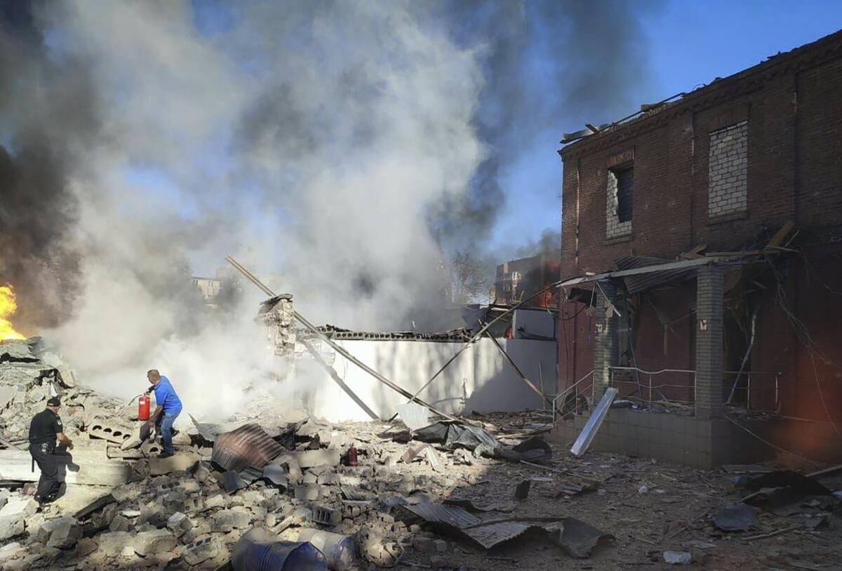 People work to extinguish a fire surrounded by rubble and smoke