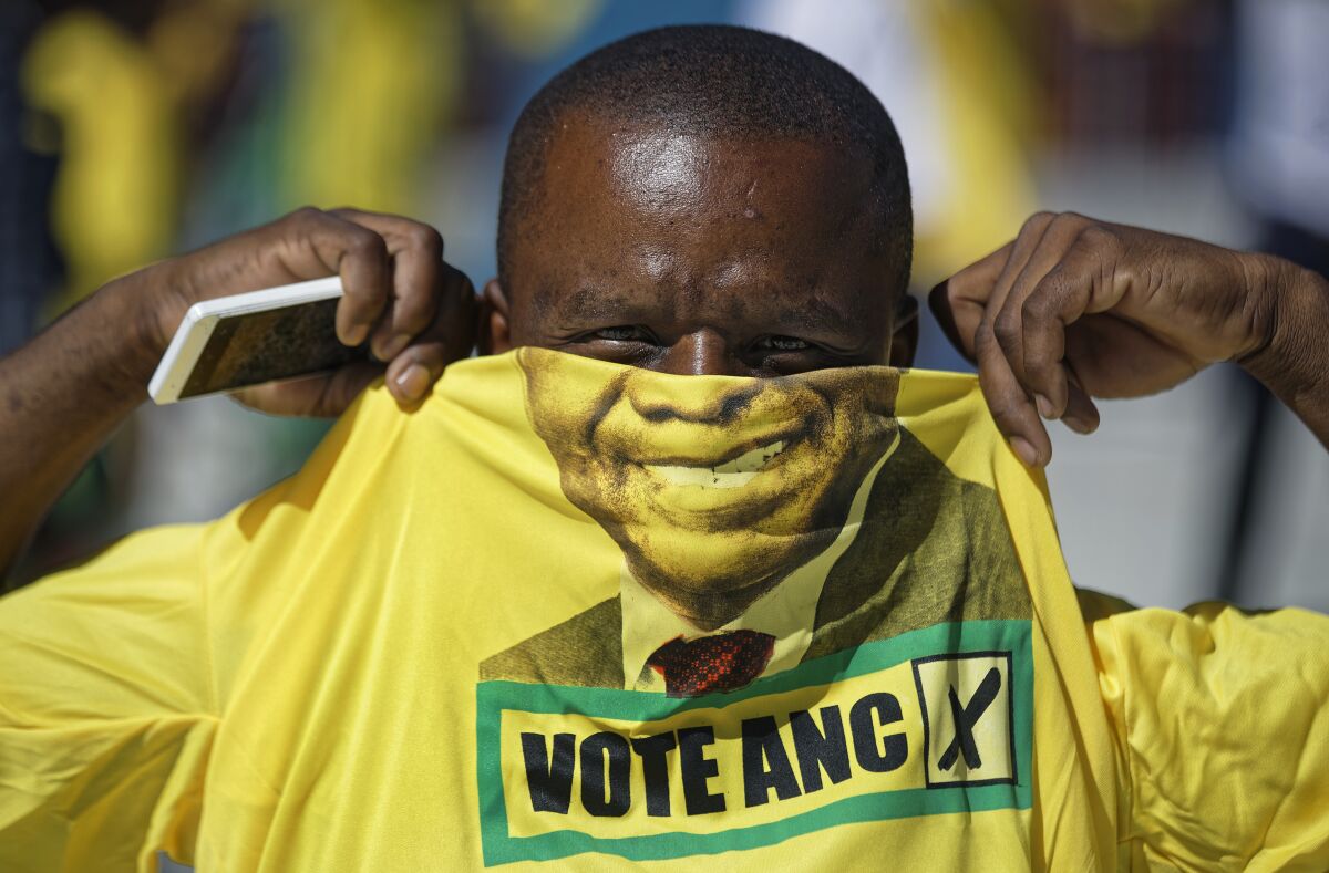 FILE - A supporter of the ruling African National Congress (ANC) holds up a T-shirt of President Cyril Ramaphosa as he attends their final election rally at Ellis Park stadium in Johannesburg, South Africa, May 5, 2019. South African President Cyril Ramaphosa is challenged Wednesday Jan. 5, 2022 to take decisive action against the corruption documented in a judicial report presented to the leader and made public. The report recommends criminal prosecution against several high-profile officials often taking orders from former President Jacob Zuma during his presidency from 2009 to 2018.(AP Photo/Ben Curtis, File)