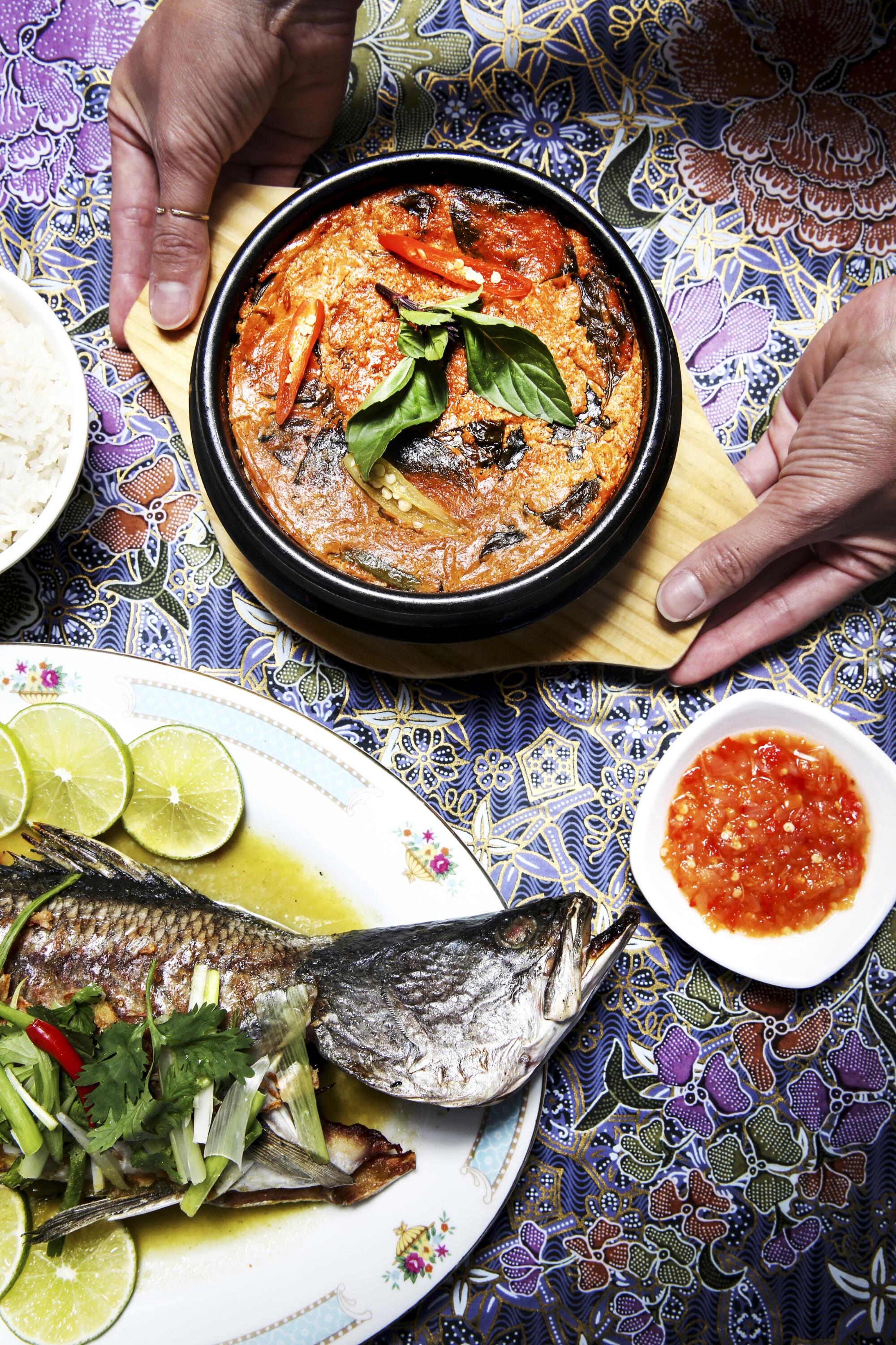 Overhead view of a variety of dishes, including fish curry and a whole fish, on a table.