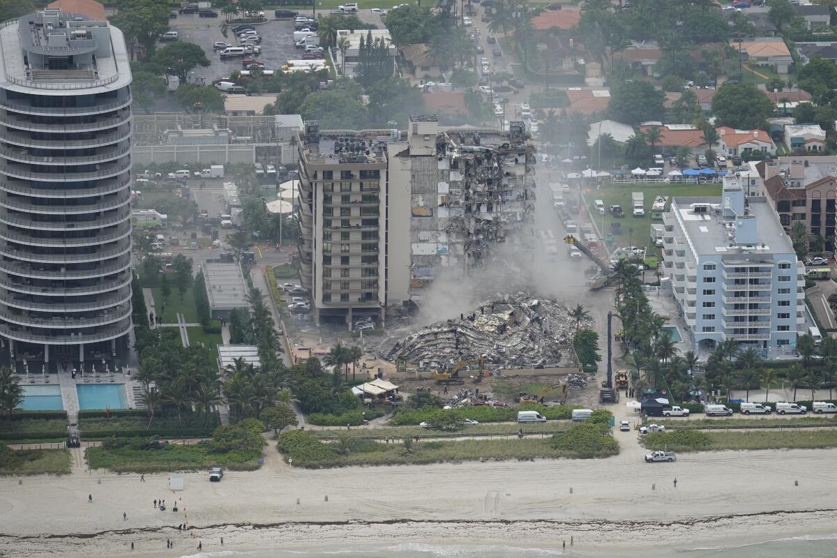 Rubble appears in front of a partly collapsed tower among a row of beachfront buildings.