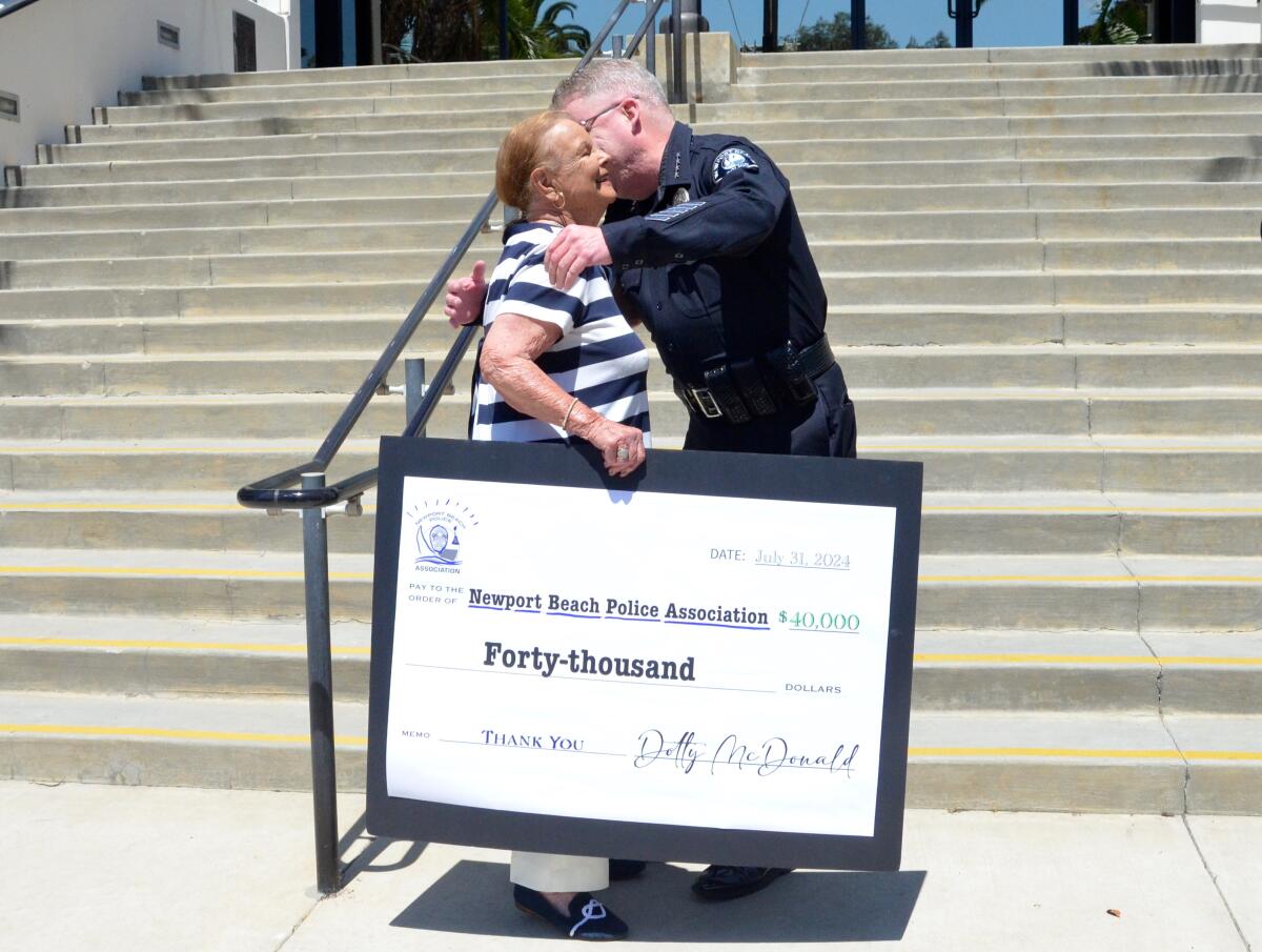 Dotty McDonald holds a large facsimile of a $40,000 check as Police Chief Cartwright gives her a hug.