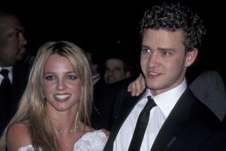 Britney Spears wearing a white and brown dress and Justin Timberlake wearing a suit are posing for photos 