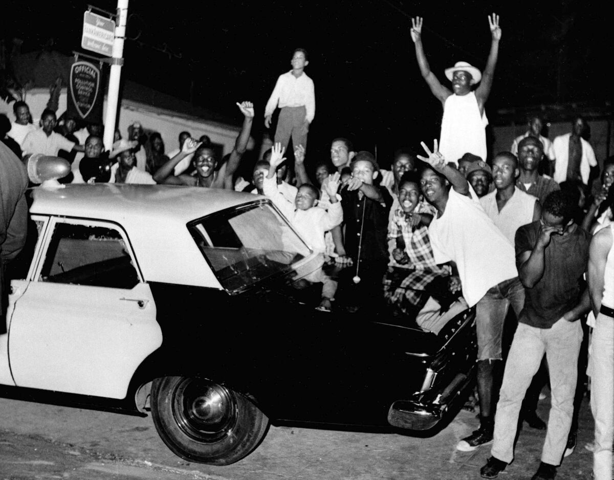 FILE - In this Aug. 12, 1965, file photo, demonstrators push against a police car in the Los Angeles area of Watts. Watts has been associated with an uprising in 1965 that led to burned-down buildings and bloodshed. But when some protests against racial injustice in 2020 devolved into vandalism and looting, Watts has been peaceful. (AP Photo/File)