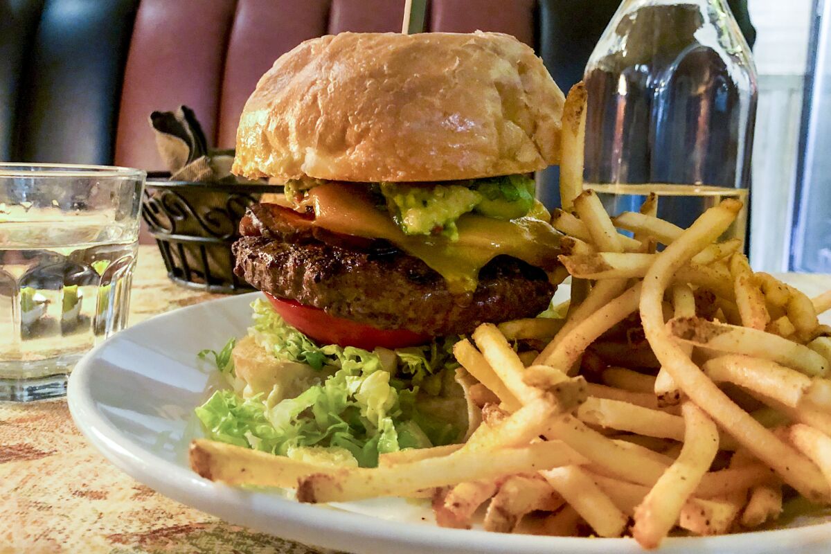 A hamburger stacked with bacon and avocado, on a plate with french fries.