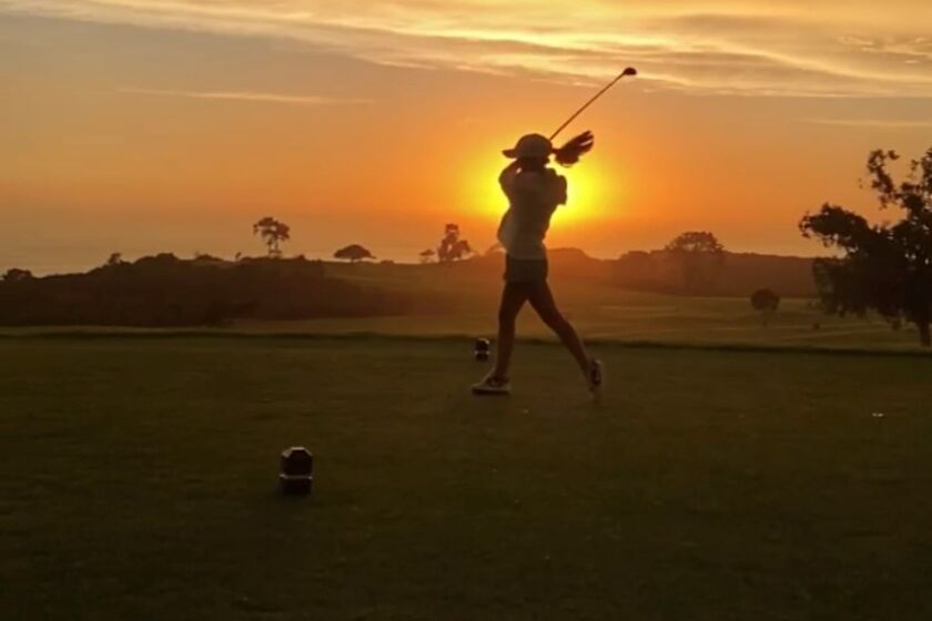 A golfer at Torrey Pines Golf Course takes a swing against the setting sun.