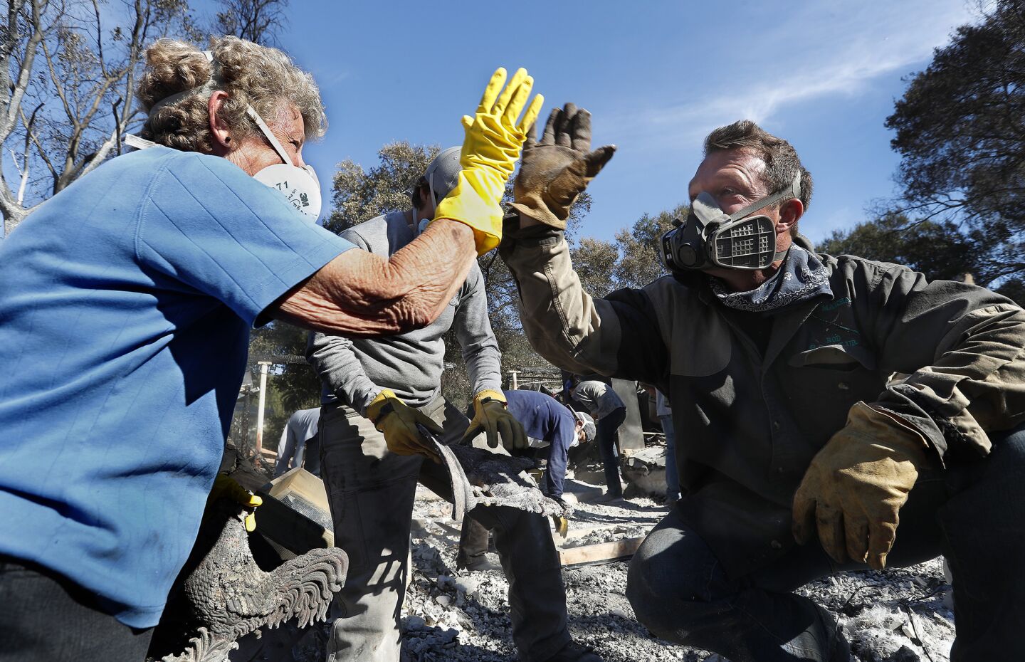 Leona Mote, left, high-fives Trevor Quirk as a team of volunteers helps sift through the rubble of her home near Ojai that burnt to the ground in the Thomas fire. Among the items recovered were her husband's wedding band, jewelry and part of a coin collection.