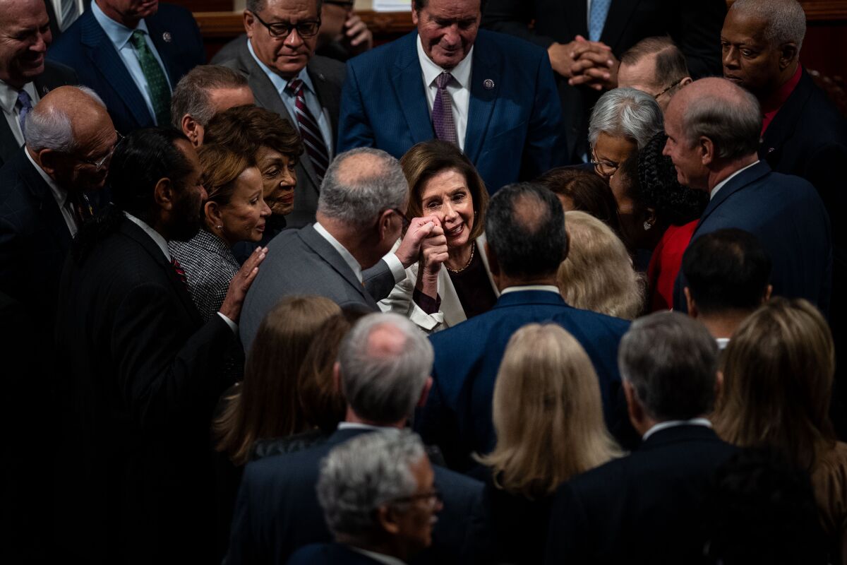 Nancy Pelosi pictured from above surrounded by a crowd of lawmakers and clutching one man's hand