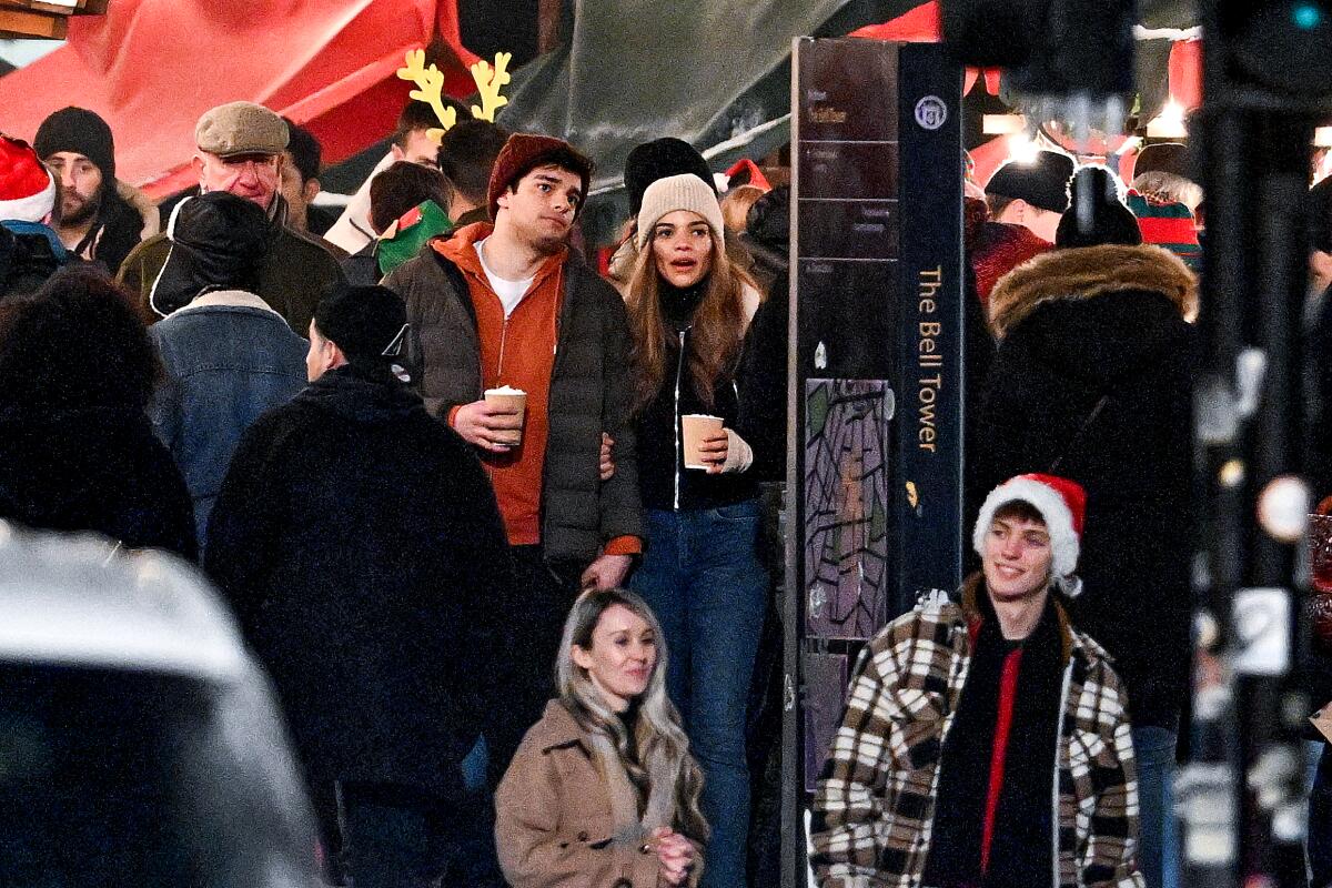 A man and a woman holding coffee cups stand among a crowd of people in winter clothing 