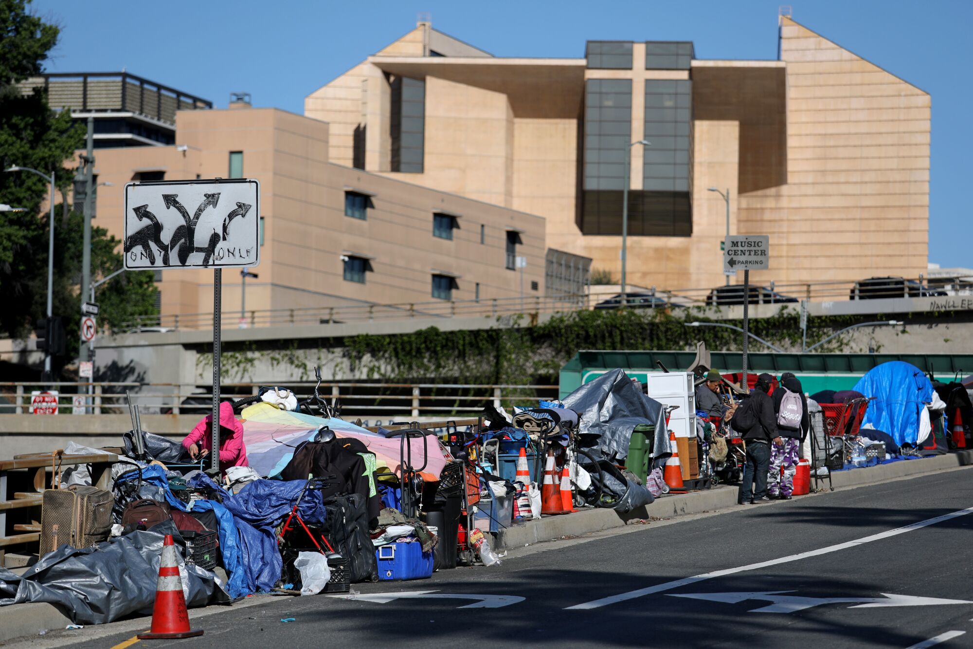 A sidewalk is crowded with bags, suitcases, carts and tarps.