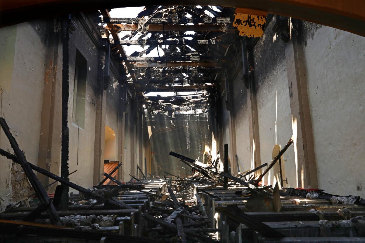 Sunlight beams through the destroyed roof onto charred pews inside the San Gabriel Mission Church