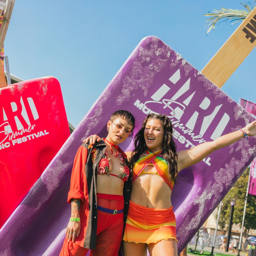 Two people wearing colorful clothes and posing in front of Hard Summer signs shaped like ice pops.