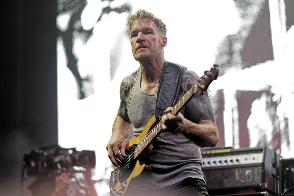 A man in a gray shirt holding a bass guitar
