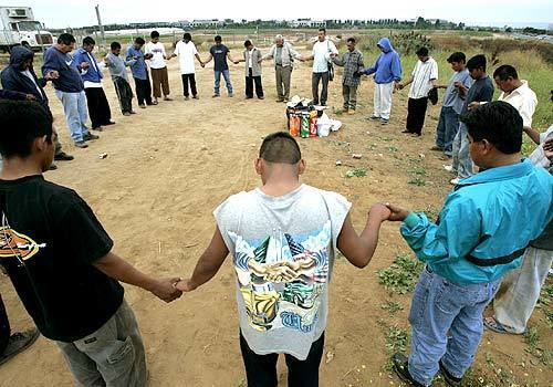 Farmworkers join hands in prayer at their camp in Carlsbad, in north San Diego County. Local churches and volunteers provide spiritual support, food and clothing.