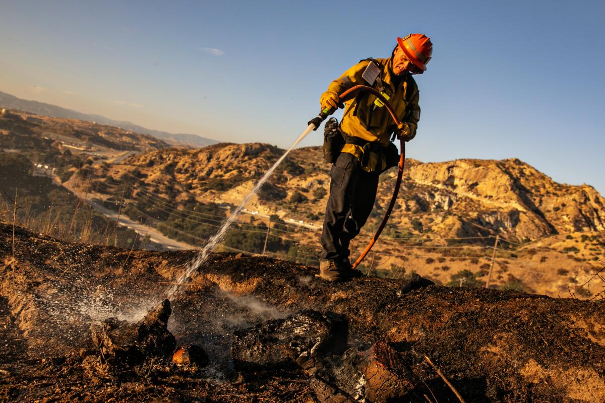 Amid a rocky landscape, a firefighter uses a hose to point a stream of water at the ground.