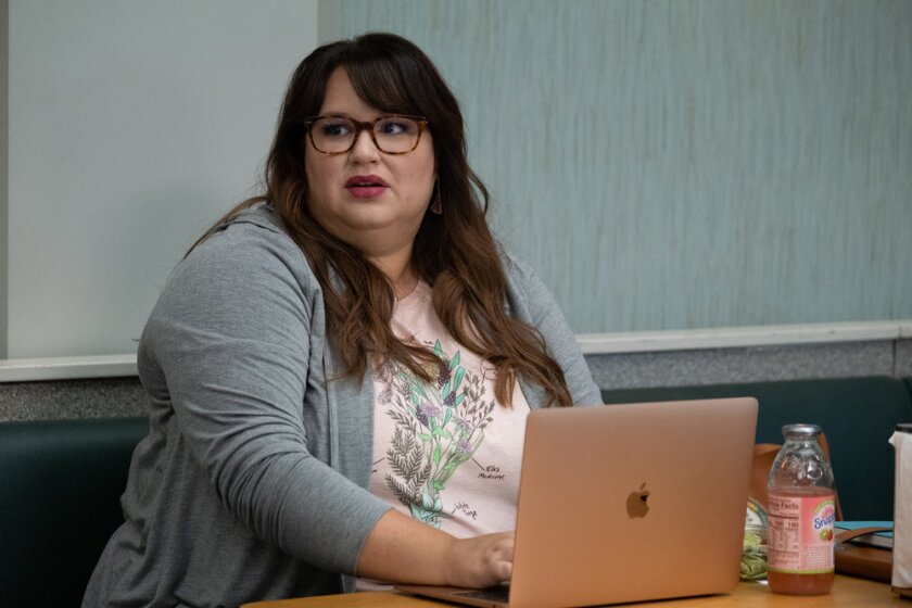 A woman wearing glasses sits while looking up from a laptop computer