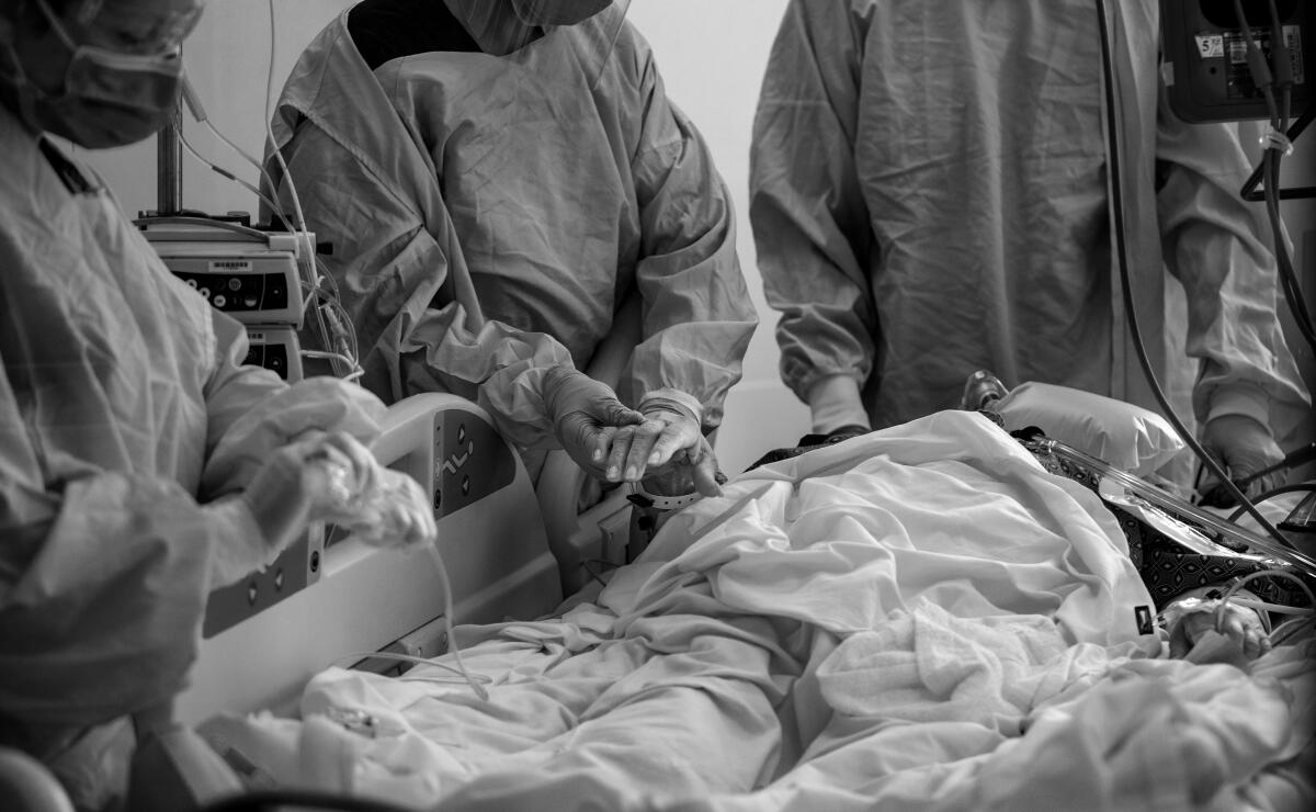 Black and white image of doctors and nurses attending a swaddled patient; one nurse holds the patients hand   