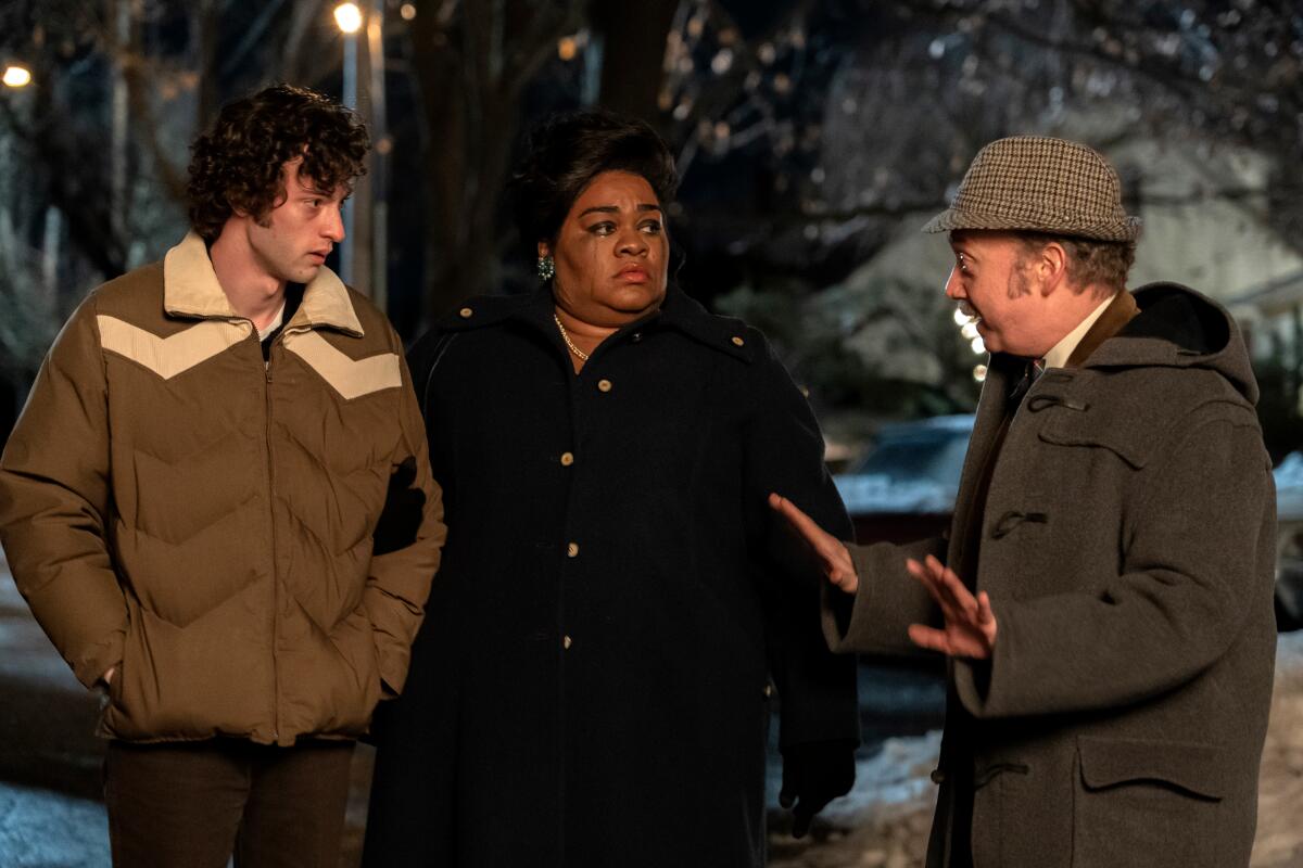 A young man and an older man walk outside with a woman between them, all in warm coats in "The Holdovers."
