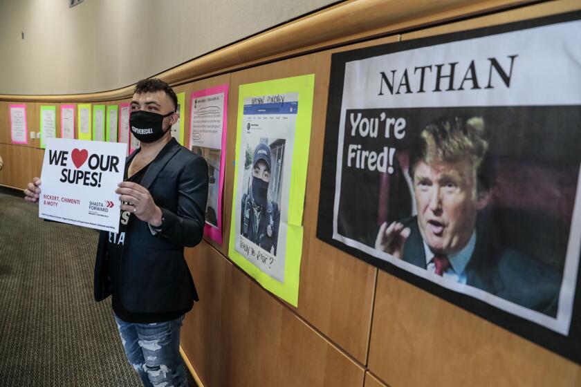 Redding, CA, Tuesday, May 11, 2021 - Nathan Pinkney, aka Nathan Blaze, poses for photos in front of a wall filled with posters showing his past social media posts and traffic tickets at the Shasta County Board of Supervisors meeting. The display was placed by Richard Gallardo, who supports the recall of certain board members who said he was looking to discredit Pinkney, a self-described comediean/provacateur who supports the embattled board members. Pinkney was hoping to serve a restraining order against Carlos Zapata, a member of a local militia, and recall leader, who allegedly punched him a week earlier. Zapata did not attend the meeting. (Robert Gauthier/Los Angeles Times)