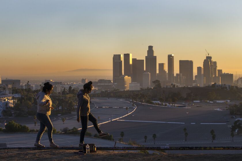 With the L.A. skyline in the background, Stacey Martinez and Jessica Arellano balance on an old irrigation pipe on a dry slope at Angels Point in Elysian Park. LA’s temperature is expected to rise 5 degrees by midcentury, and public health officials are worried about what that’ll mean for Angelenos.
