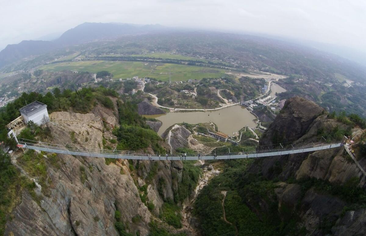 Tourists walk on a suspension bridge made of glass at the Shiniuzhai National Geological Park on September 24, 2015 in Pingjiang County, China.