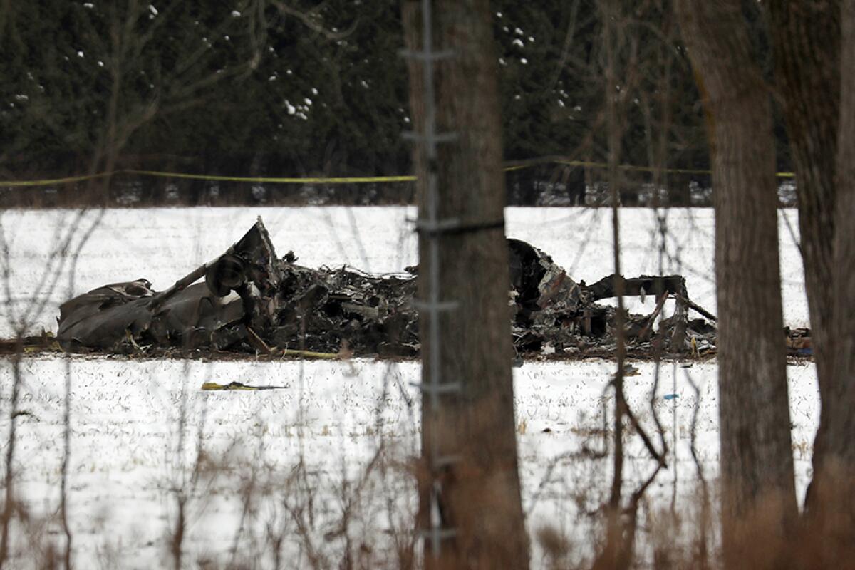 The wreckage of a helicopter lies in a snow-covered field.