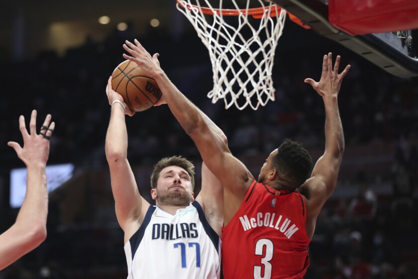 El jugador de los Mavericks de Dallas Luka Doncic recibe una falta de CJ McCollum, de los Trail Blazers de Portland, durante la primera mitad del juego de la NBA que enfrentó a ambos equipos, en Portland, Oregon, el 26 de enero de 2022. (AP Foto/Amanda Loman)