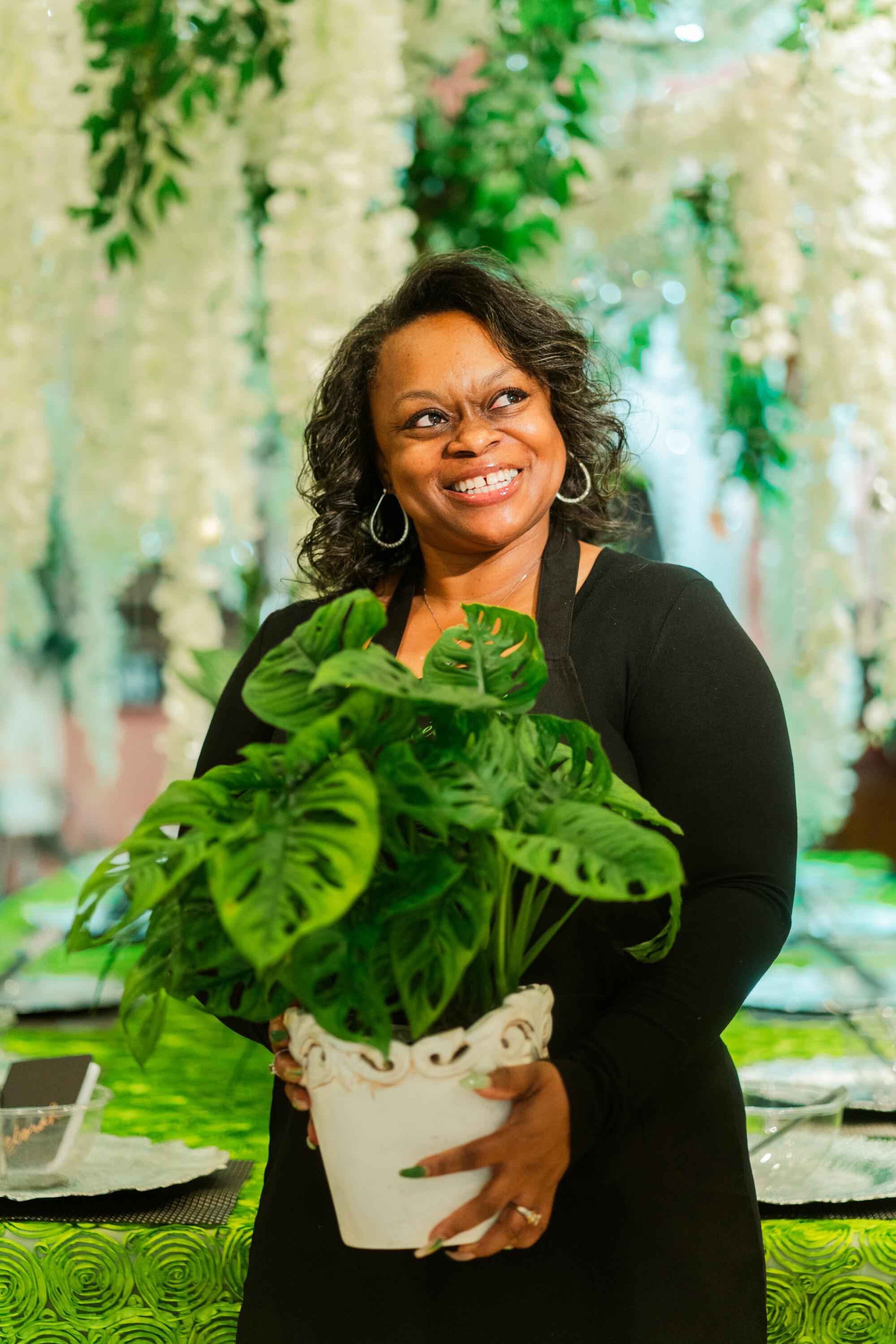 A smiling woman stands holding a healthy houseplant in a white pot