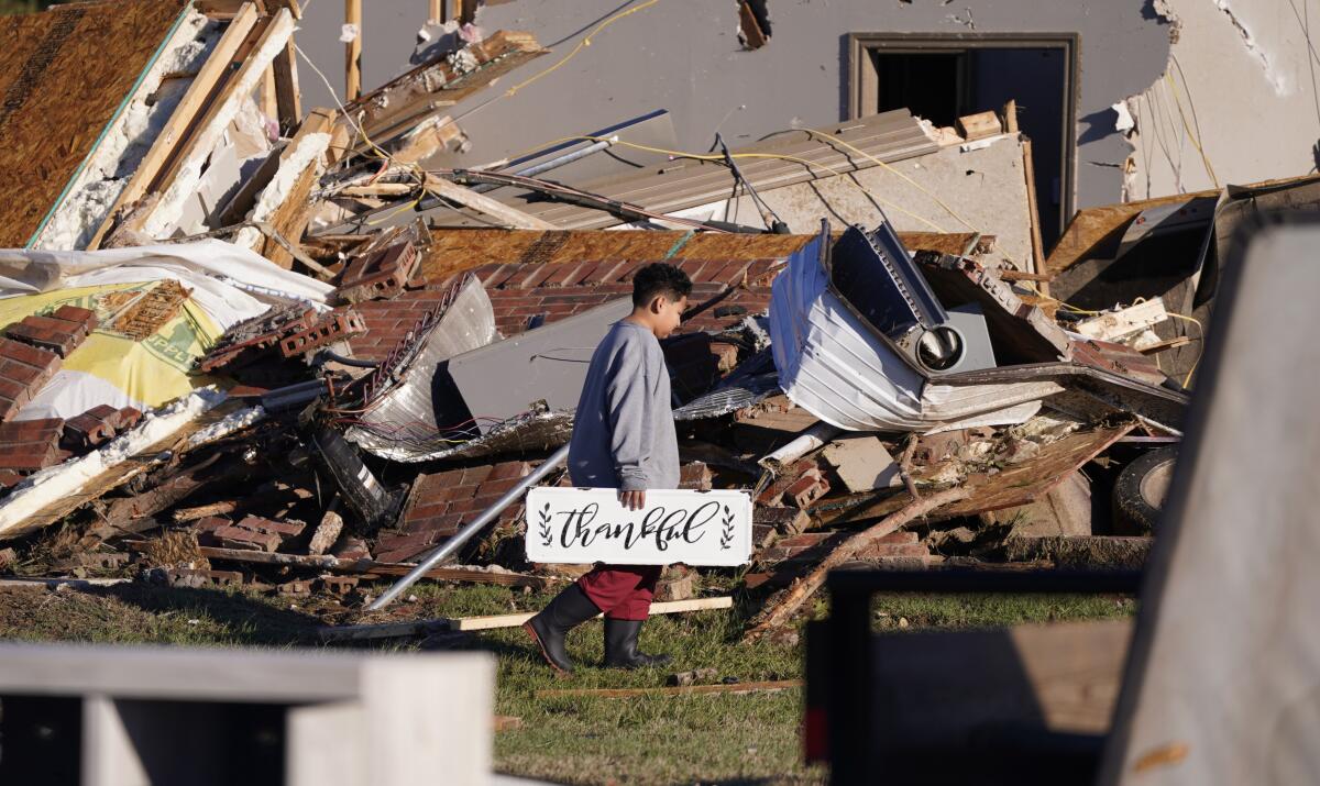 A boy holding a sign that reads "thankful" outside his family's destroyed home